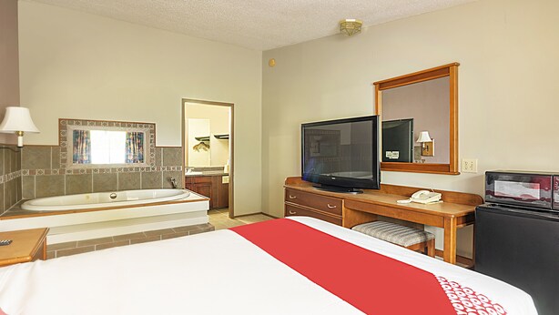 Una habitación de hotel con una cama grande, televisión, escritorio con teléfono y bañera.