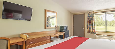A hotel room with a bed, a desk with a television, a mirror, and a window with curtains.