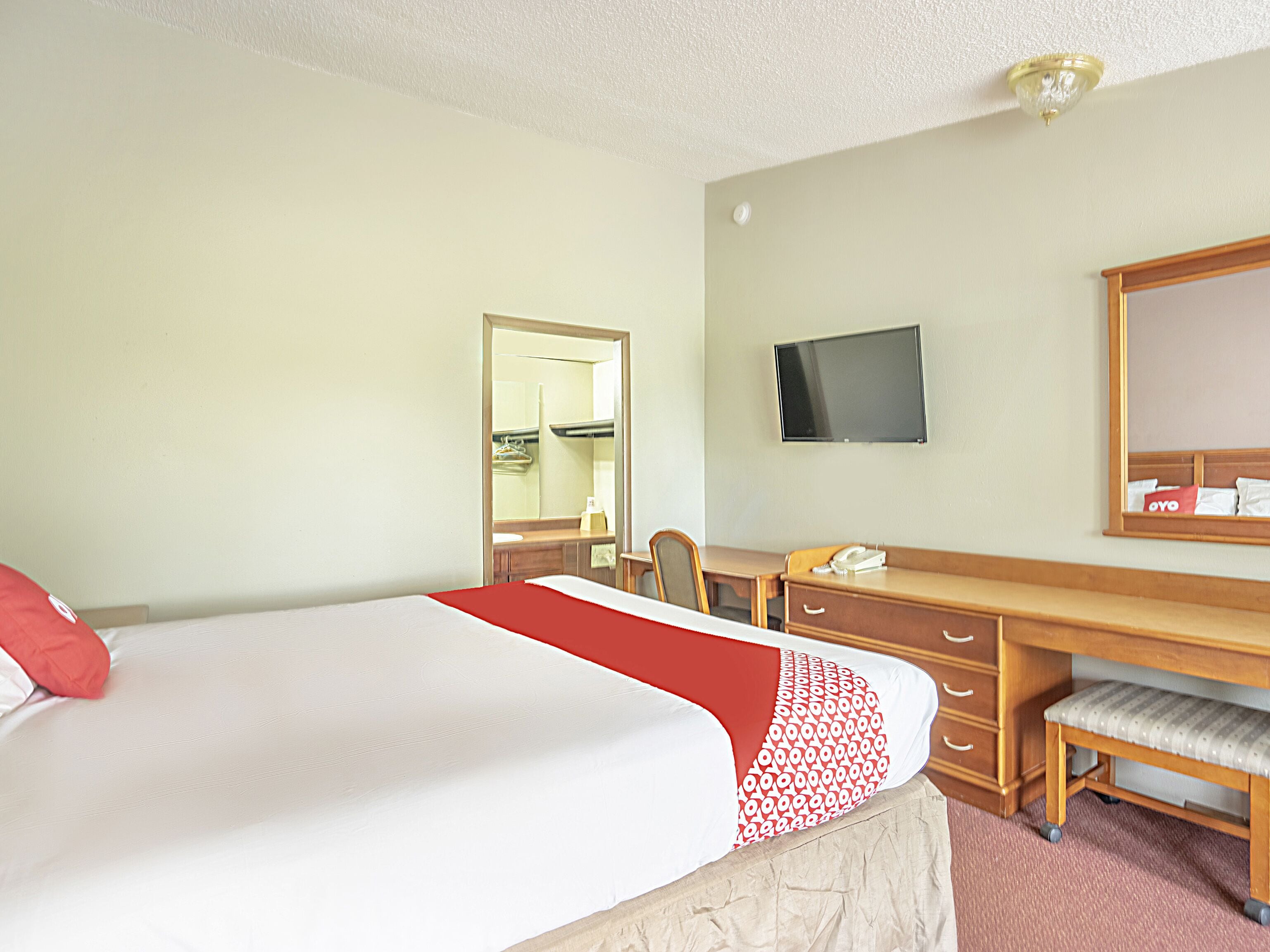 Una habitación de hotel con una cama, un escritorio, una silla, un televisor y un espejo.