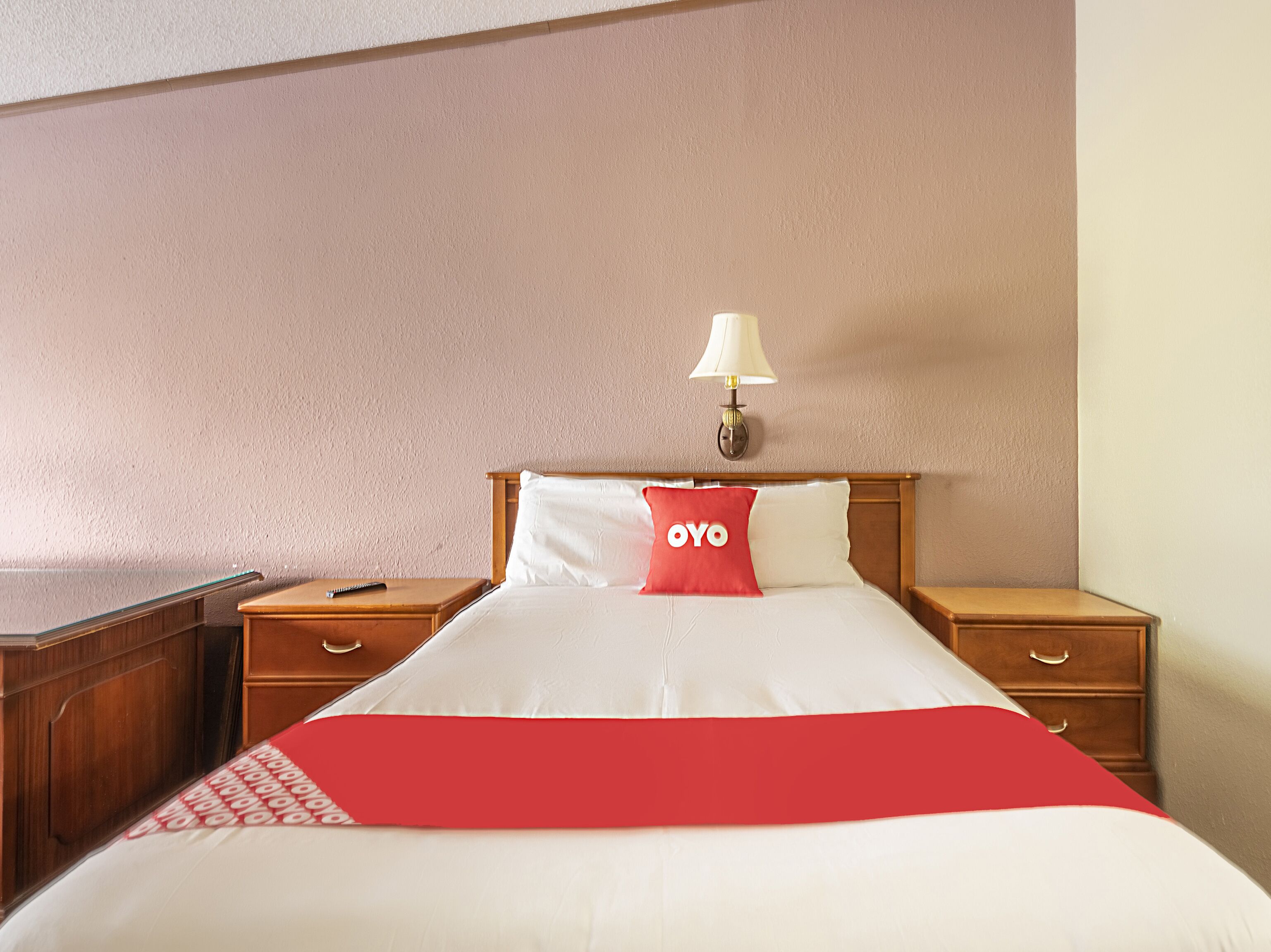 A hotel room with a bed, two wooden nightstands, a lamp, and a red and white bedspread.