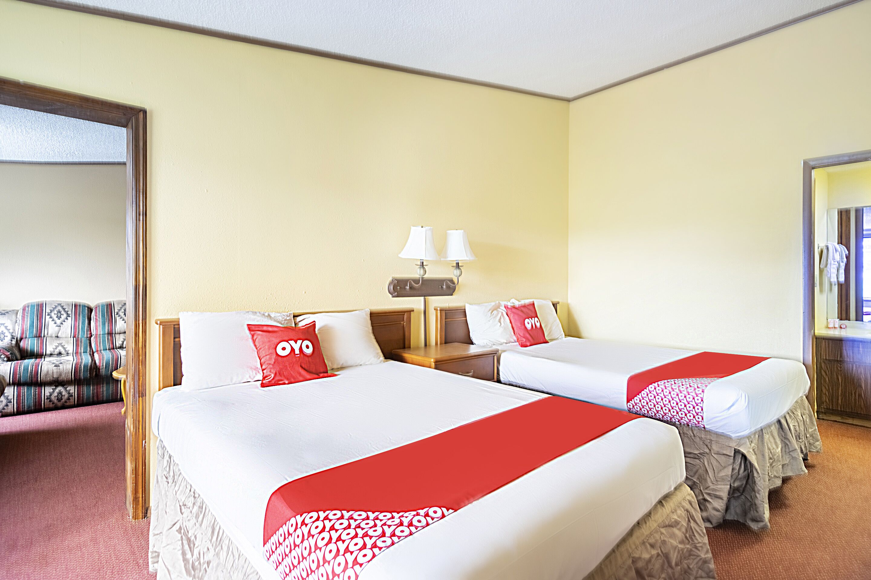 Habitación de hotel con dos camas, un sofá y un baño visible a través de una puerta abierta.
