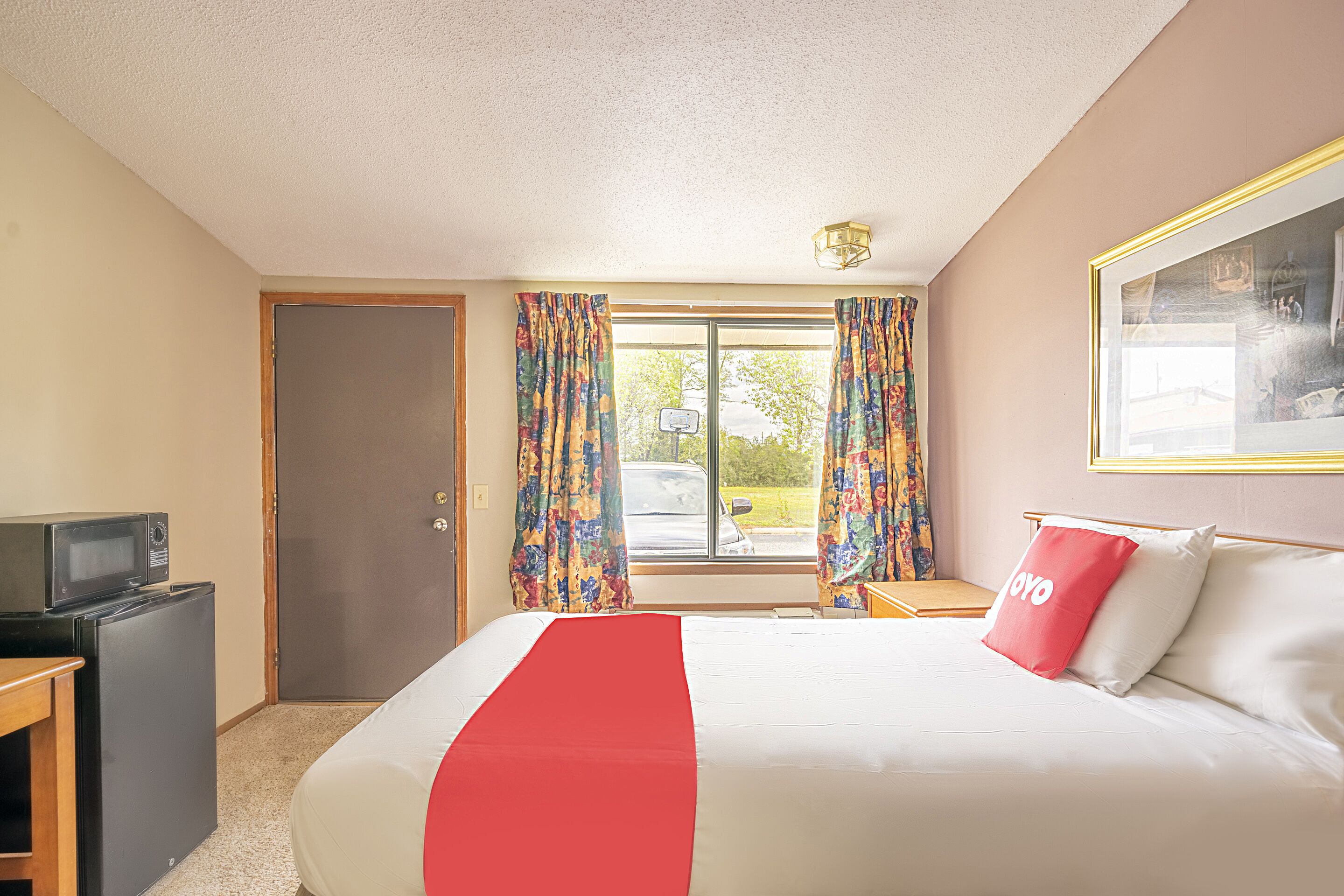 A hotel room with a bed, a television, a small refrigerator, and a window with curtains.