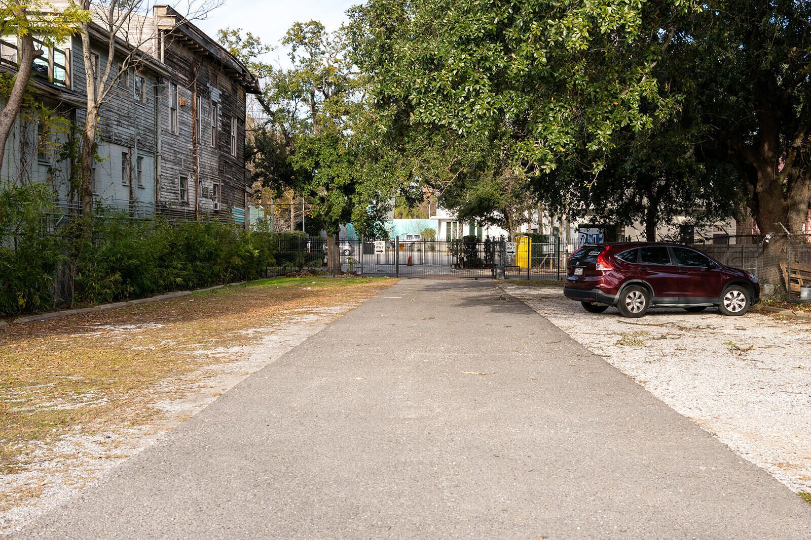 A paved pathway flanked by trees and a parked car.