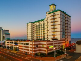 Un hotel de varios pisos con una destacada torre de reloj, una entrada a nivel de calle y vistas al océano.