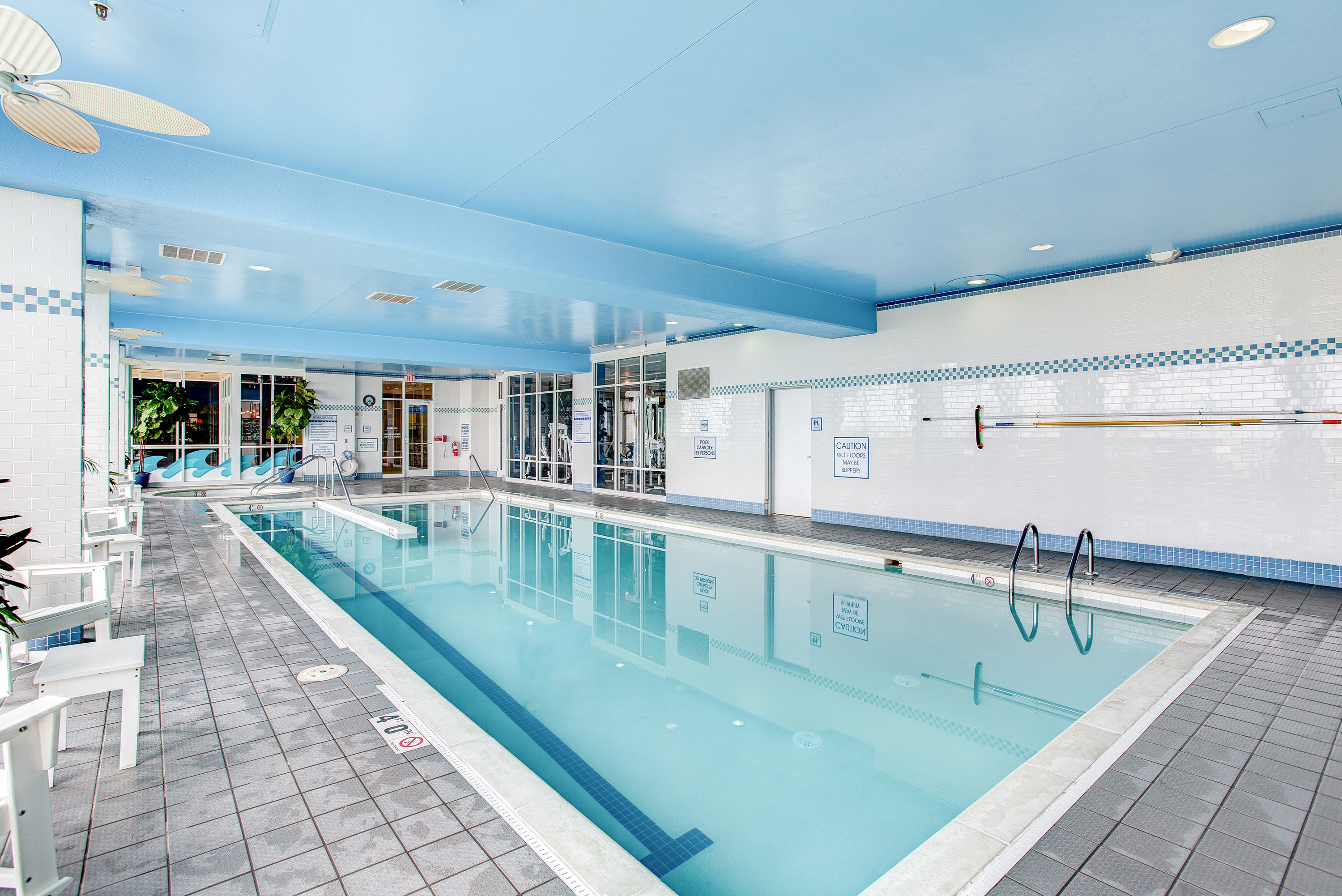 An indoor swimming pool with clear lanes, a ceiling fan, and a tiled floor.