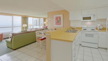 A hotel room with a kitchenette, a dining area with a green sofa, a view of the sea, and a large window.