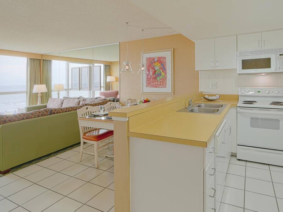 A hotel room with a kitchenette, a dining area with a green sofa, a view of the sea, and a large window.