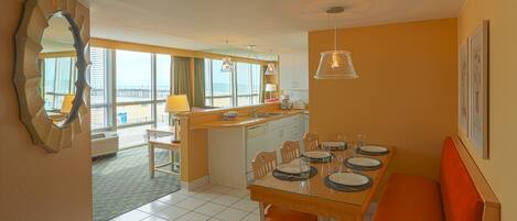 A compact hotel room with a dining area, kitchenette, and a view of the beach.
