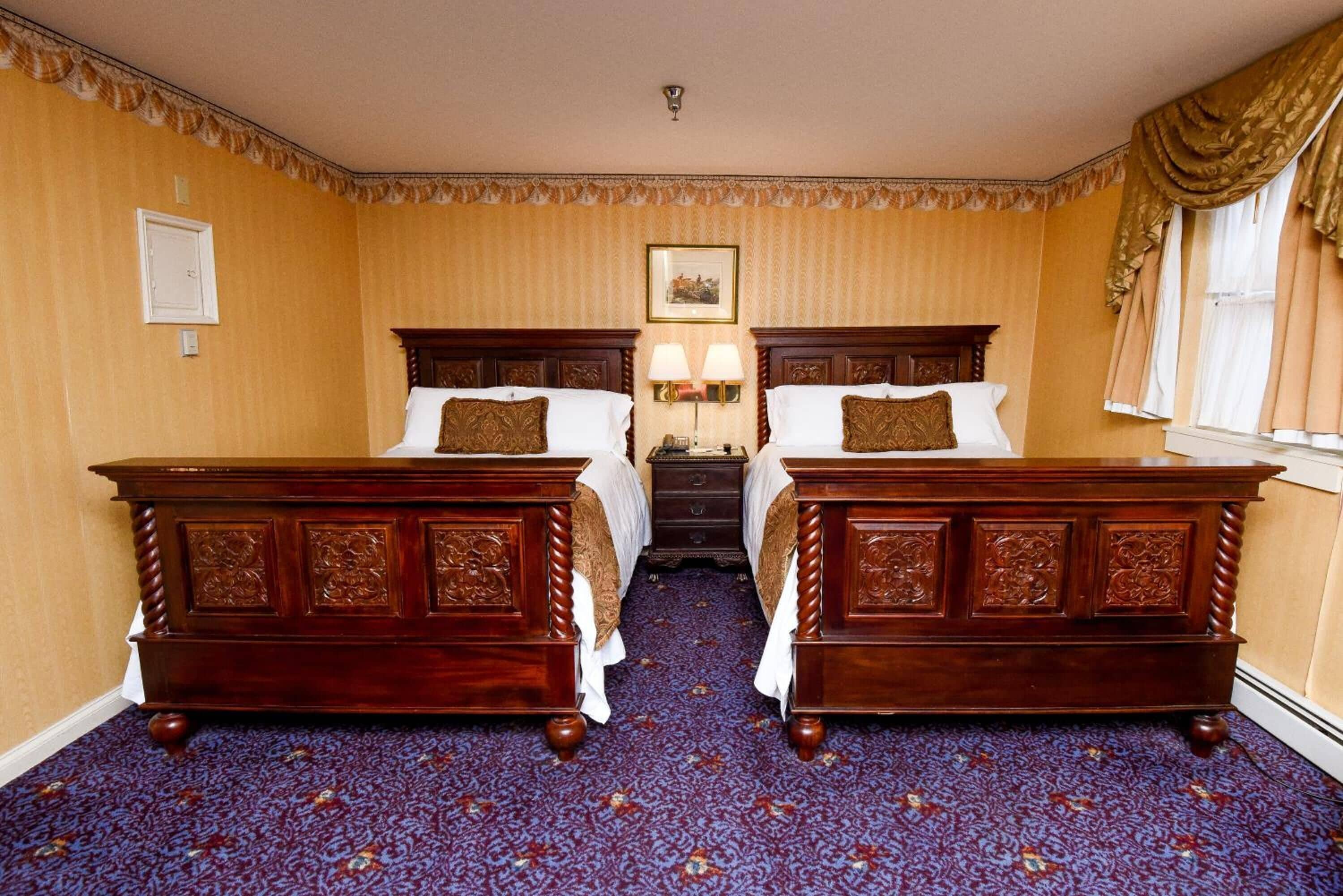 A hotel room with two wooden beds, a nightstand, a lamp, and a framed picture on the wall.