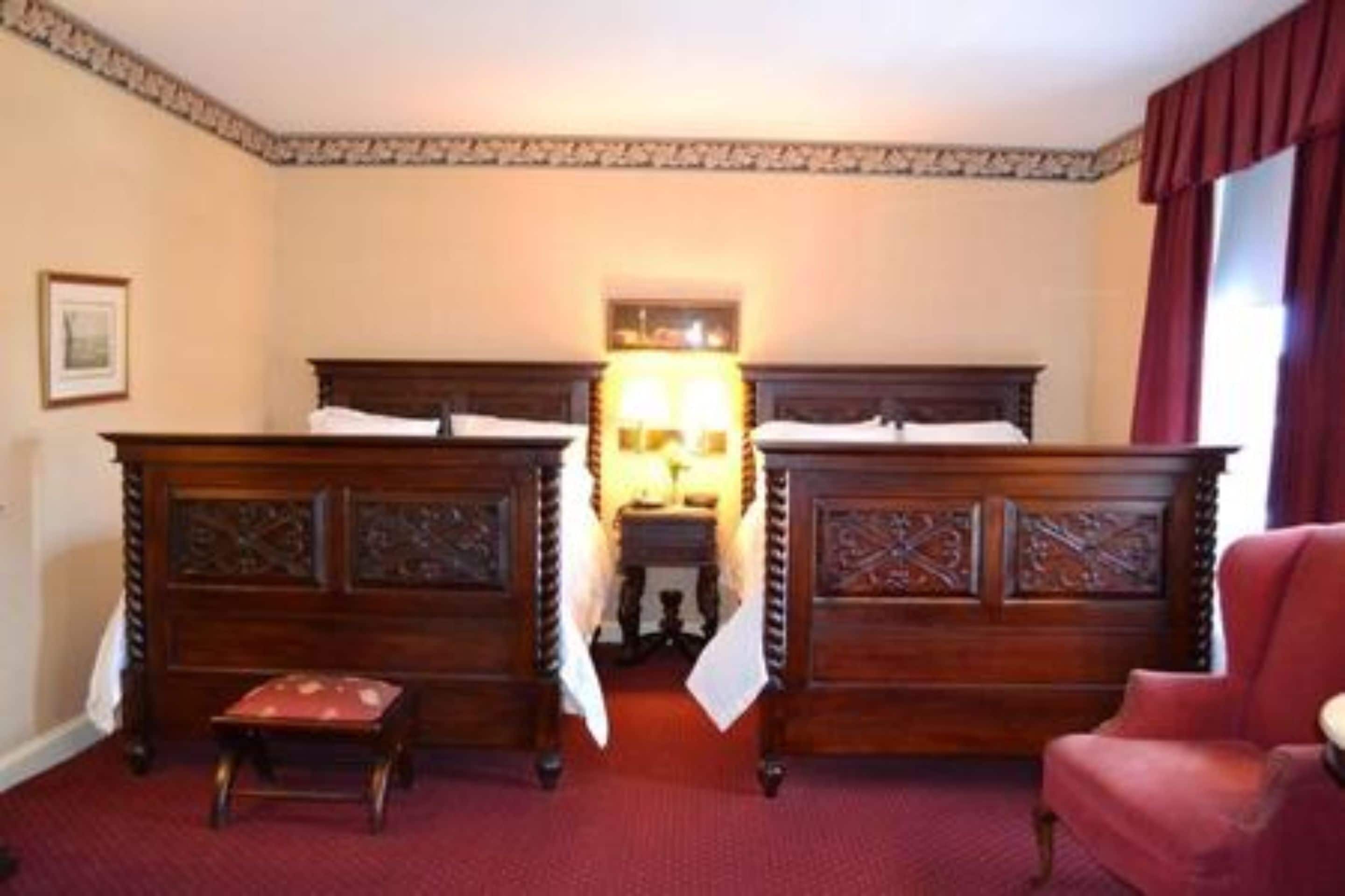 A hotel room with two wooden beds, a red chair, and a carpeted floor.