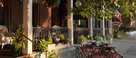 Un edificio de ladrillo con porche, plantas en macetas y una bicicleta estacionada afuera.
