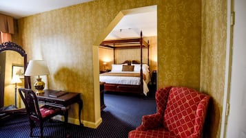 Una habitación de hotel con una cama con dosel, un escritorio con lámpara y un sillón rojo.