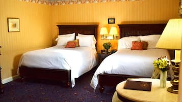 A hotel room with two beds, a nightstand with lamps, a small round table with a book, and a vase with flowers.
