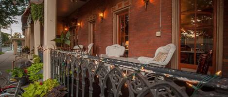 A brick building with a balcony, white chairs, and string lights.