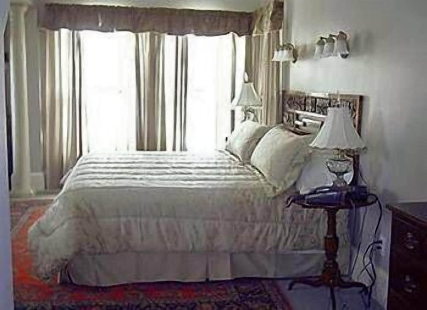 Um quarto com uma cama grande, uma mesa de cabeceira com abajur e uma janela com cortinas.