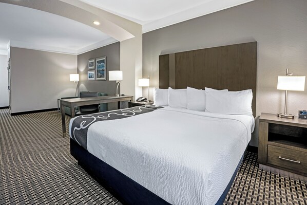A hotel room with a large bed, a desk, two bedside lamps, a chair, and a patterned carpet.