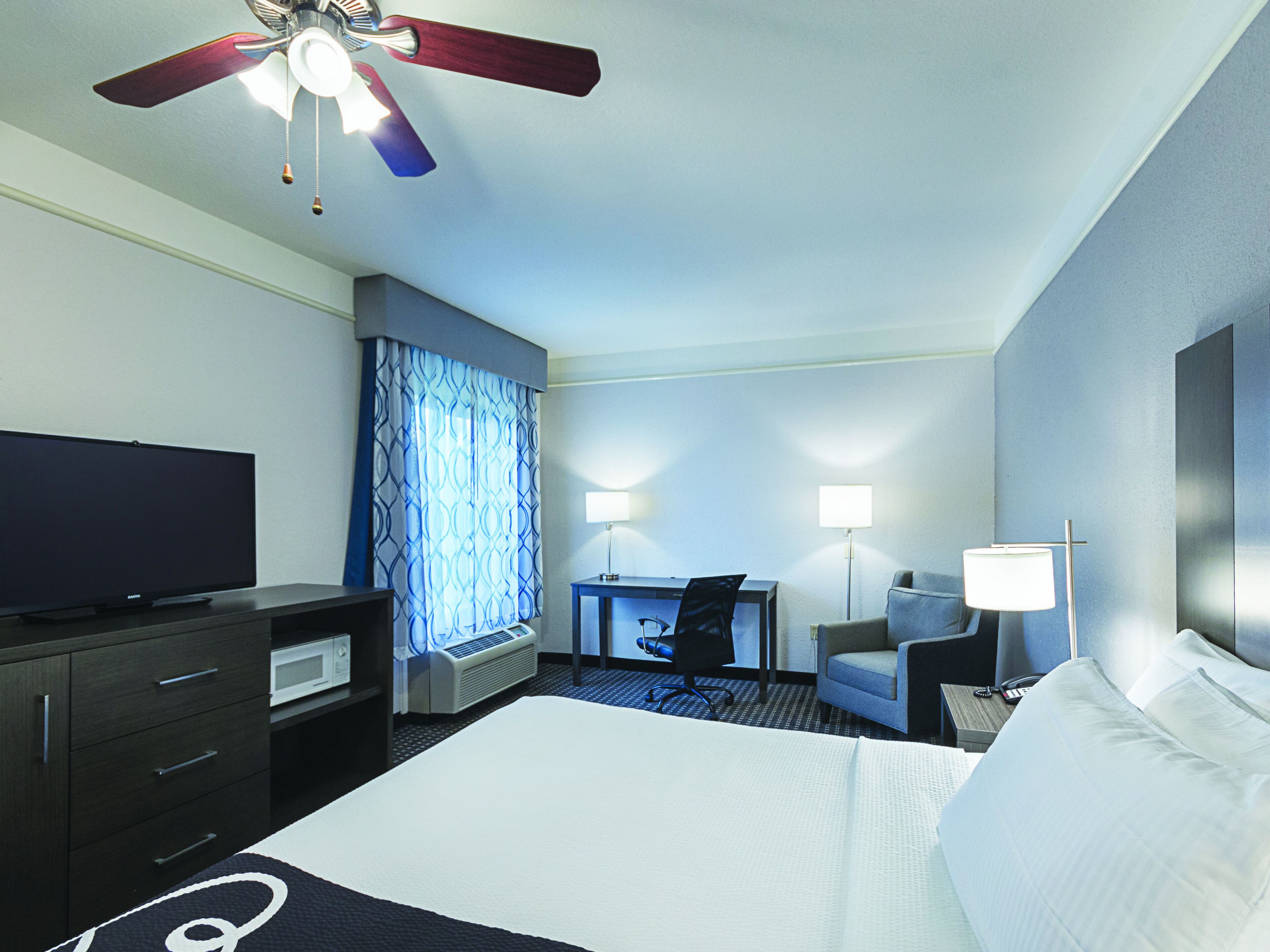 A hotel room with a bed, a desk, a chair, a television, and a ceiling fan.
