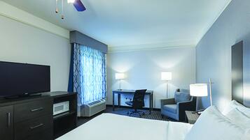 A hotel room with a bed, a desk, a chair, a television, and a ceiling fan.