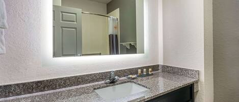 A bathroom with a granite countertop sink, a mirror, and a towel rack.