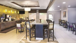 A modern hotel lobby with a central dining area, a reception desk, and a brick accent wall. - La Quinta Inn & Suites by Wyndham Tampa Bay Area-Tampa South (Tampa)