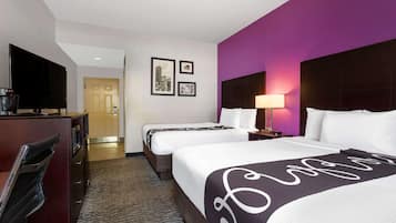 Una habitación de hotel con dos camas, un escritorio con televisor y una puerta que da a otra habitación.