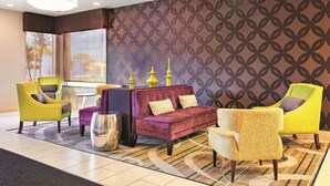 A modern hotel lobby with a patterned wall, a purple sofa, and yellow and white armchairs. - La Quinta Inn & Suites by Wyndham Tampa Bay Area-Tampa South (Tampa)