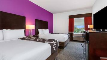 A hotel room with two beds, a desk, and a television.