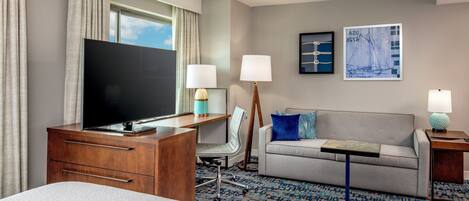A hotel room with a bed, a desk with a TV, a sofa, two lamps, and artwork on the wall.