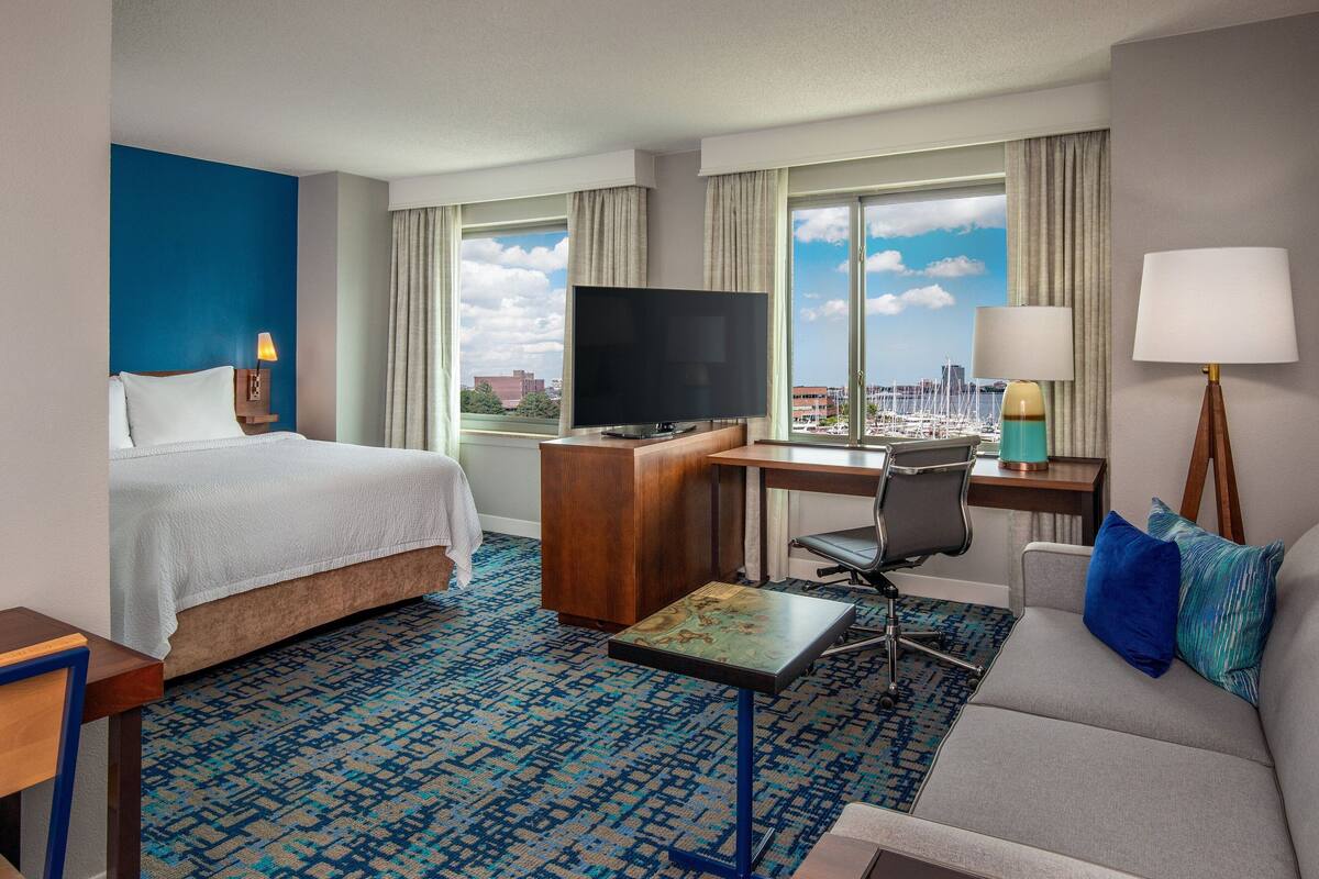 A hotel room with a bed, desk, television, and a view of the cityscape.