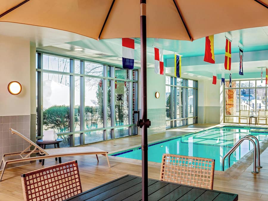 An indoor swimming pool with lounge chairs and a view of the city through large windows.