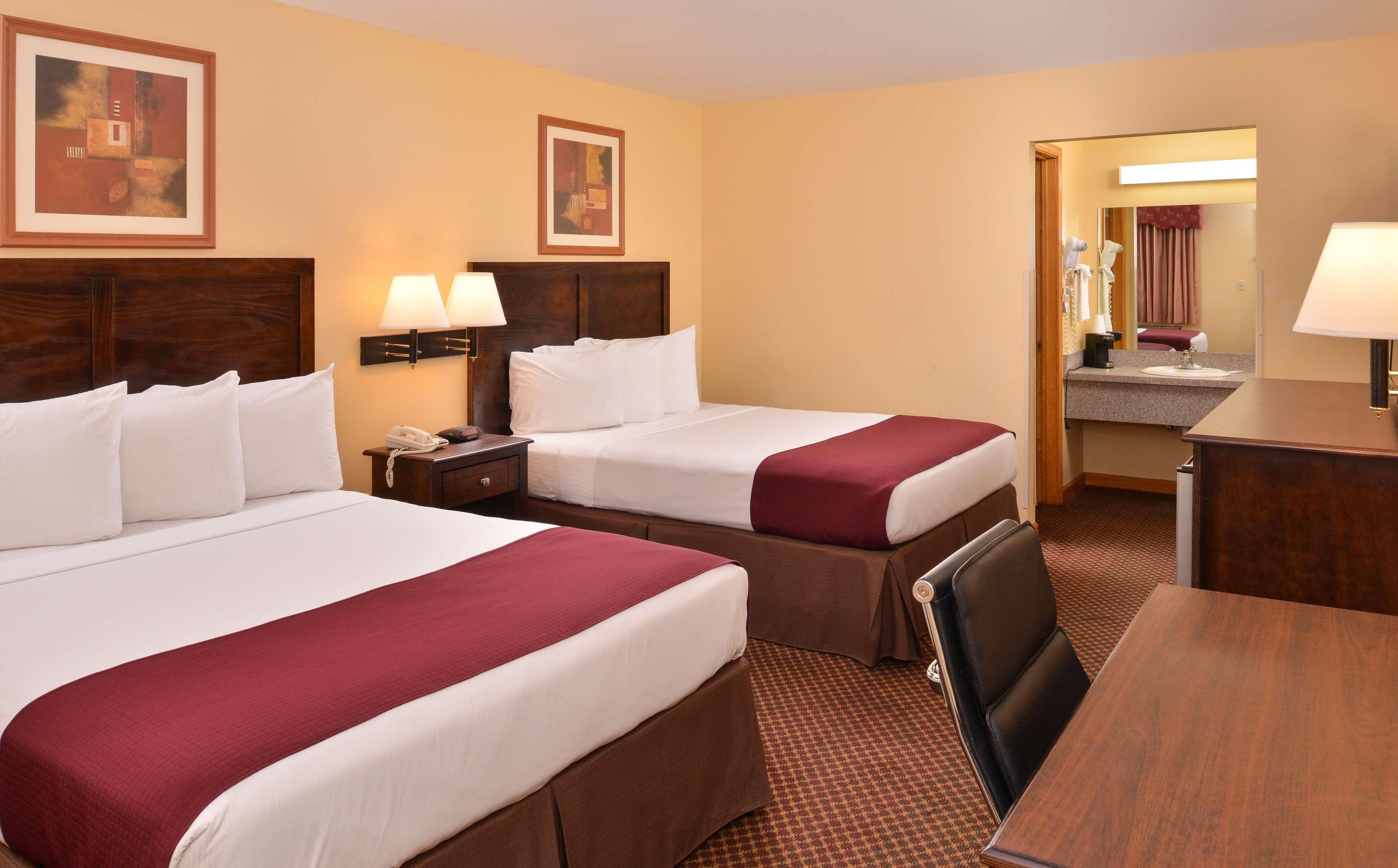 A hotel room with two beds, a desk, a chair, a nightstand, and a mirror.