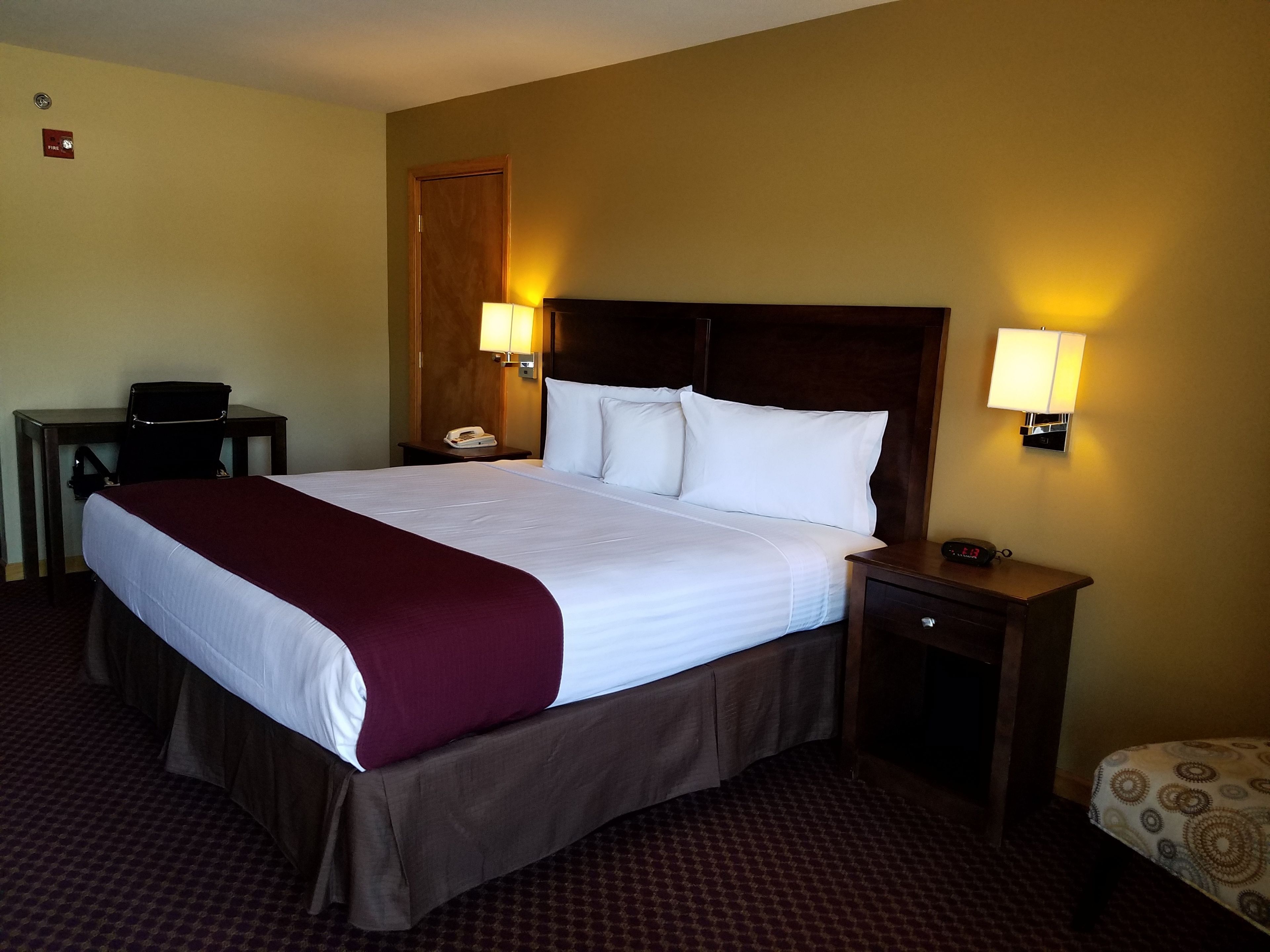 A hotel room with a large bed, two bedside lamps, a desk with a telephone, and a patterned chair.