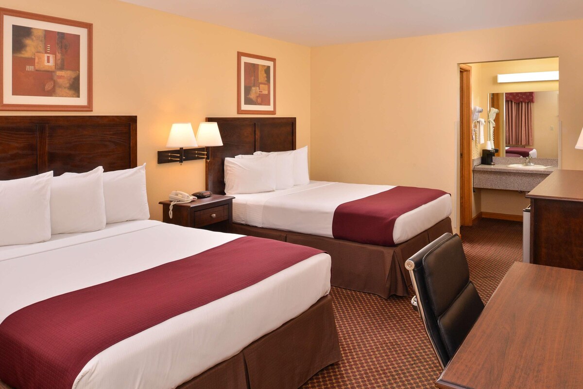 A hotel room with two beds, a desk, a chair, a nightstand, and a mirror.