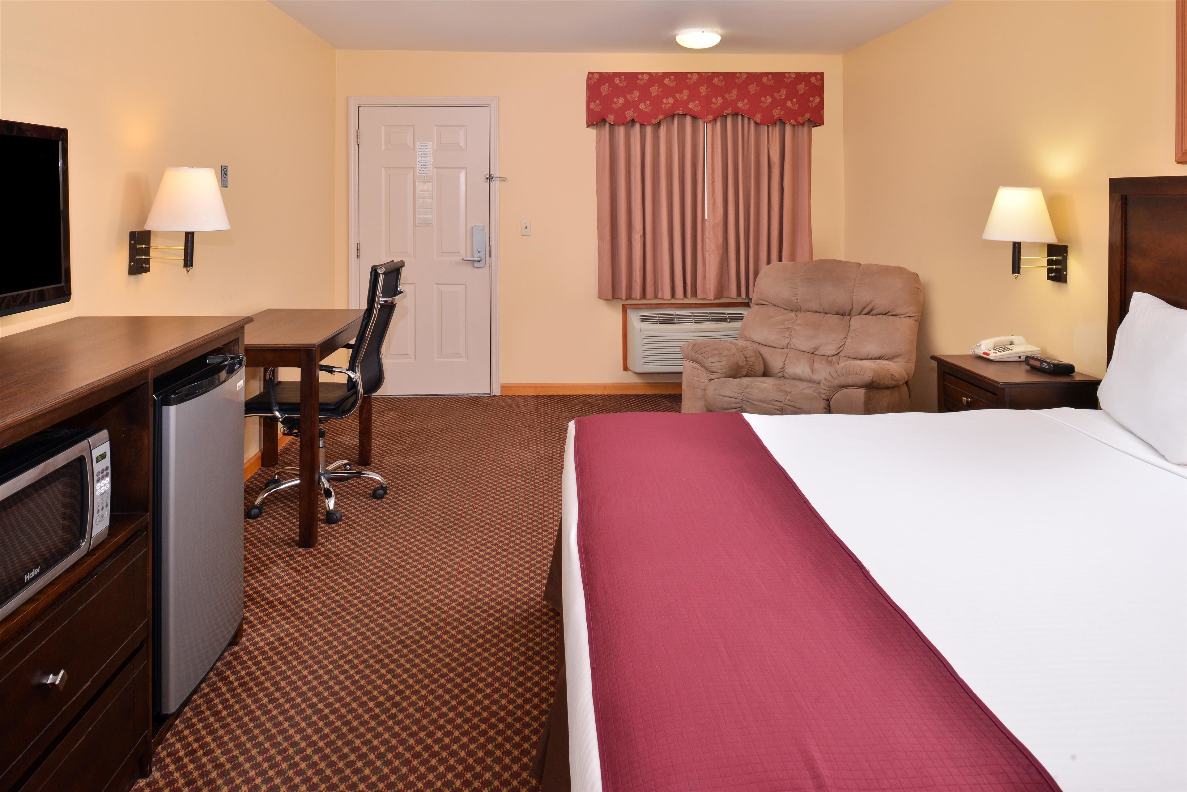 A hotel room with a bed, desk, chair, television, and a telephone.