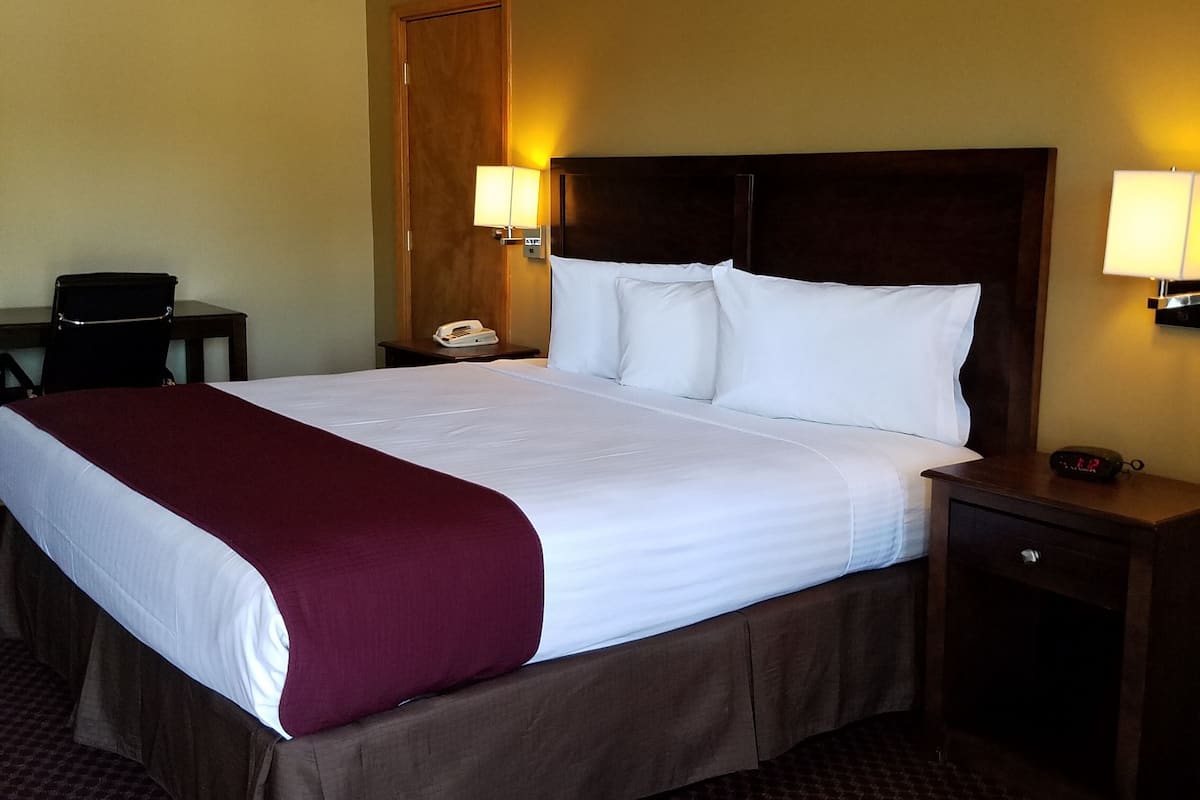 A hotel room with a large bed, two bedside tables, a nightstand, a desk, and a chair.