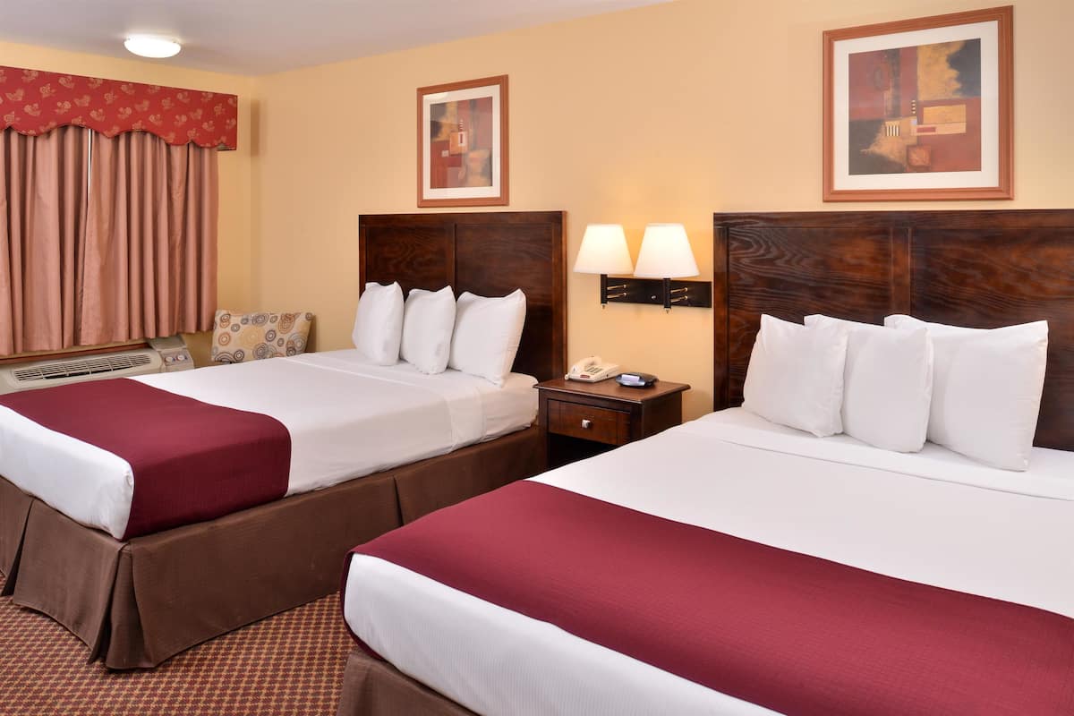 A hotel room with two beds, a bedside table with a lamp, a telephone, and a window with curtains.