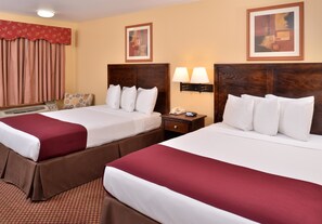 A hotel room with two beds, a bedside table with a lamp, a telephone, and a window with curtains.