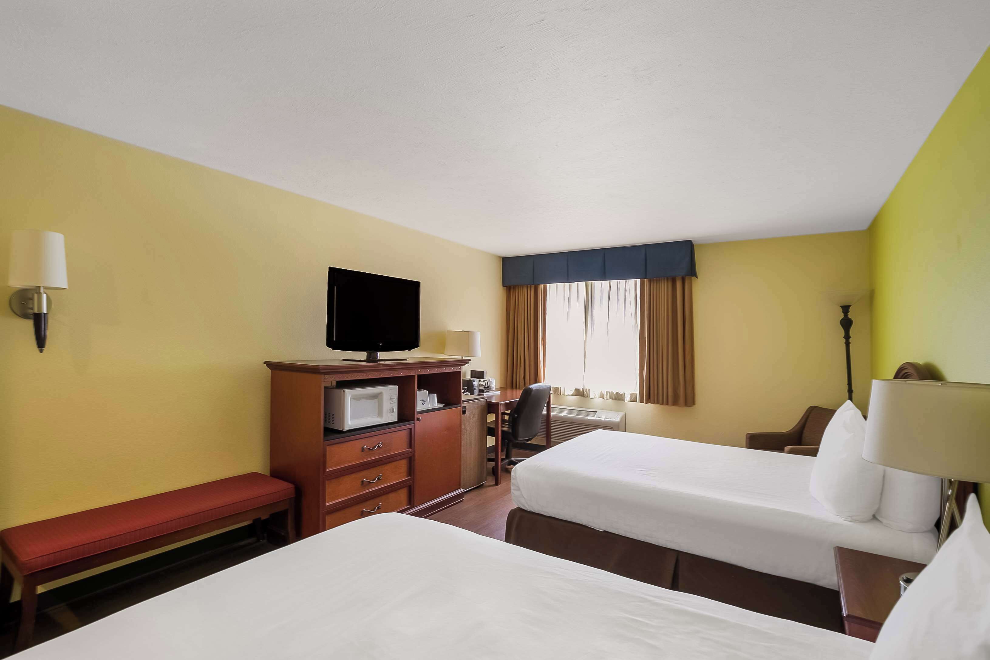 Een hotelkamer met twee bedden, een bureau met een computer, een televisie en een bankje.