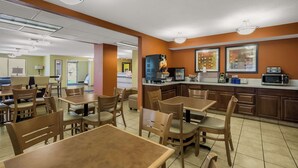 A clean, well-lit restaurant with wooden tables and chairs, a kitchen area with a microwave, and a counter with various items. - Americas Best Value Sandman Inn (La Grande)