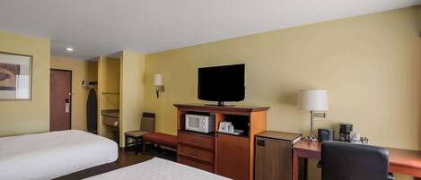 Ett hotellrum med två sängar, ett skrivbord med en dator, en tv, en mikrovågsugn och ett litet kylskåp.