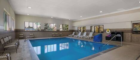 A large indoor swimming pool with clear blue water, surrounded by lounge chairs and a tiled deck.