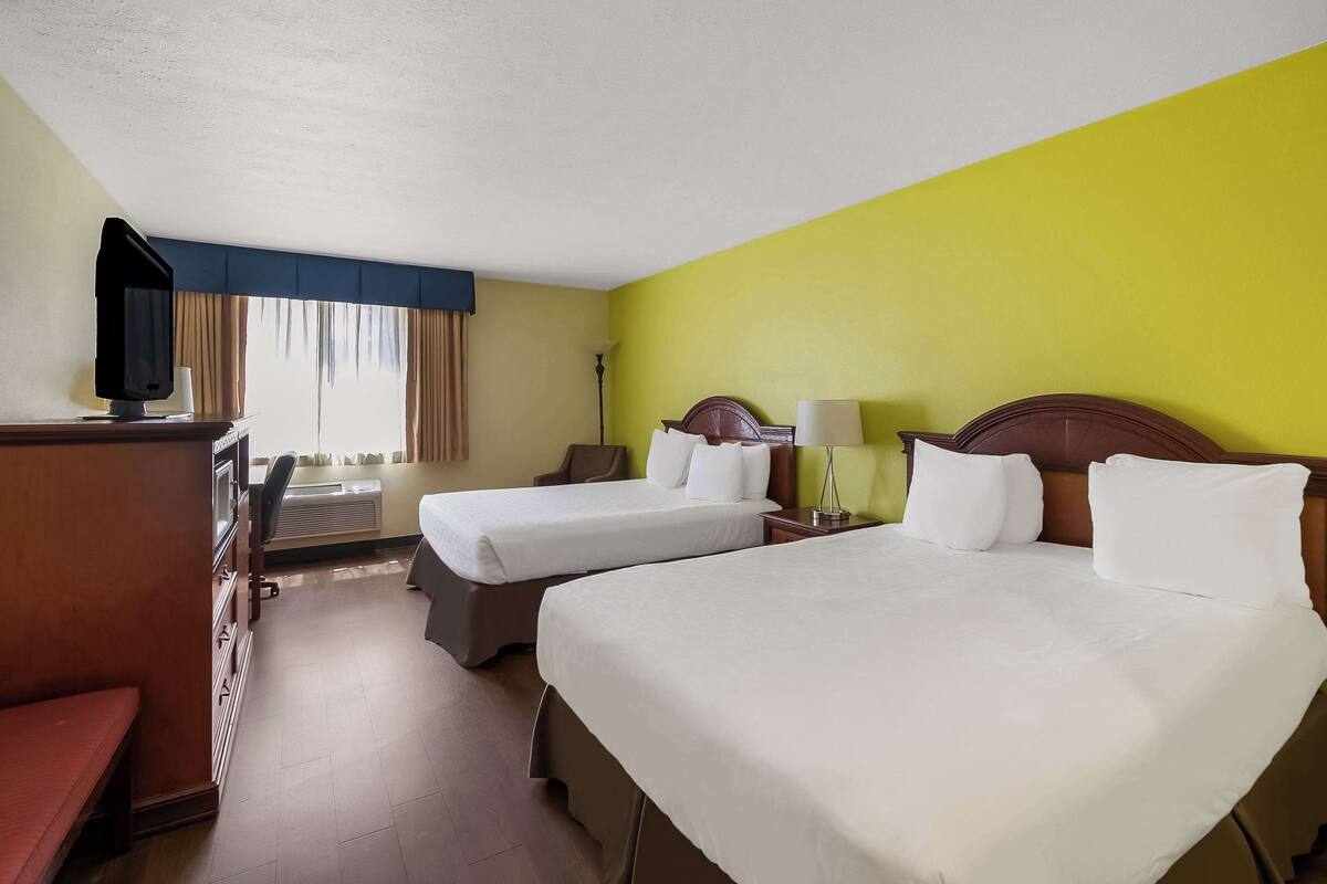 A hotel room with two beds, a desk with a television, and a bench.