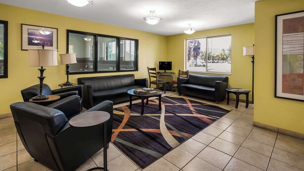 A living room with a sofa, chairs, a coffee table, and a rug. There are two windows, a door, and a wall-mounted TV. - Americas Best Value Sandman Inn (La Grande)