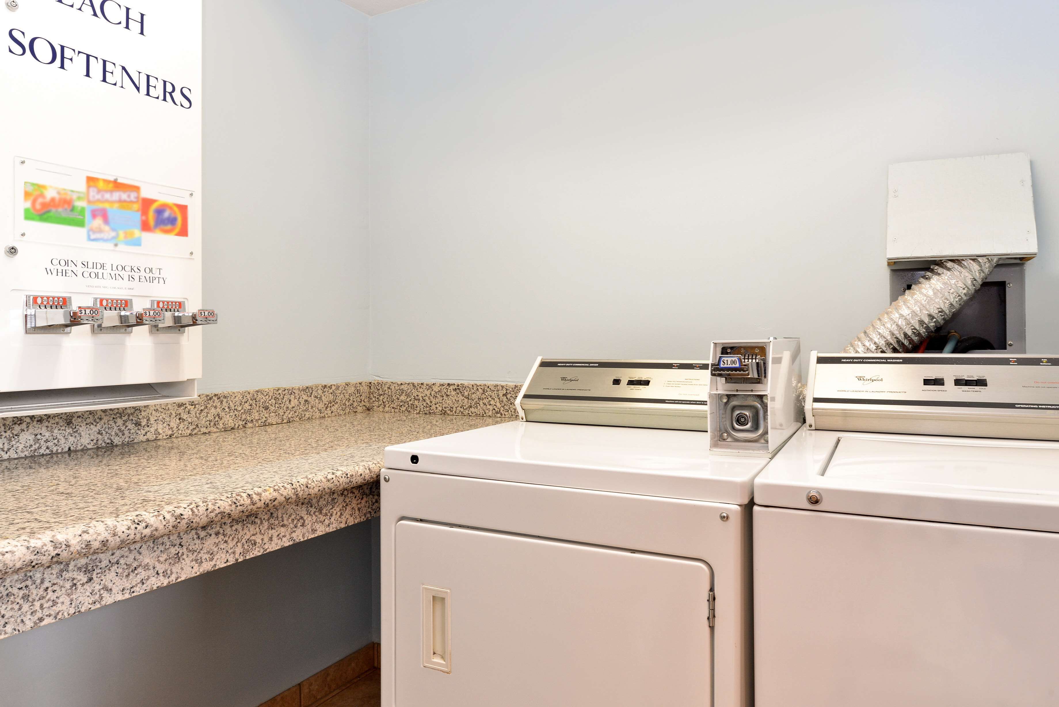 A laundry area with a coin-operated softener machine, a Whirlpool dryer, and a ventilation system.