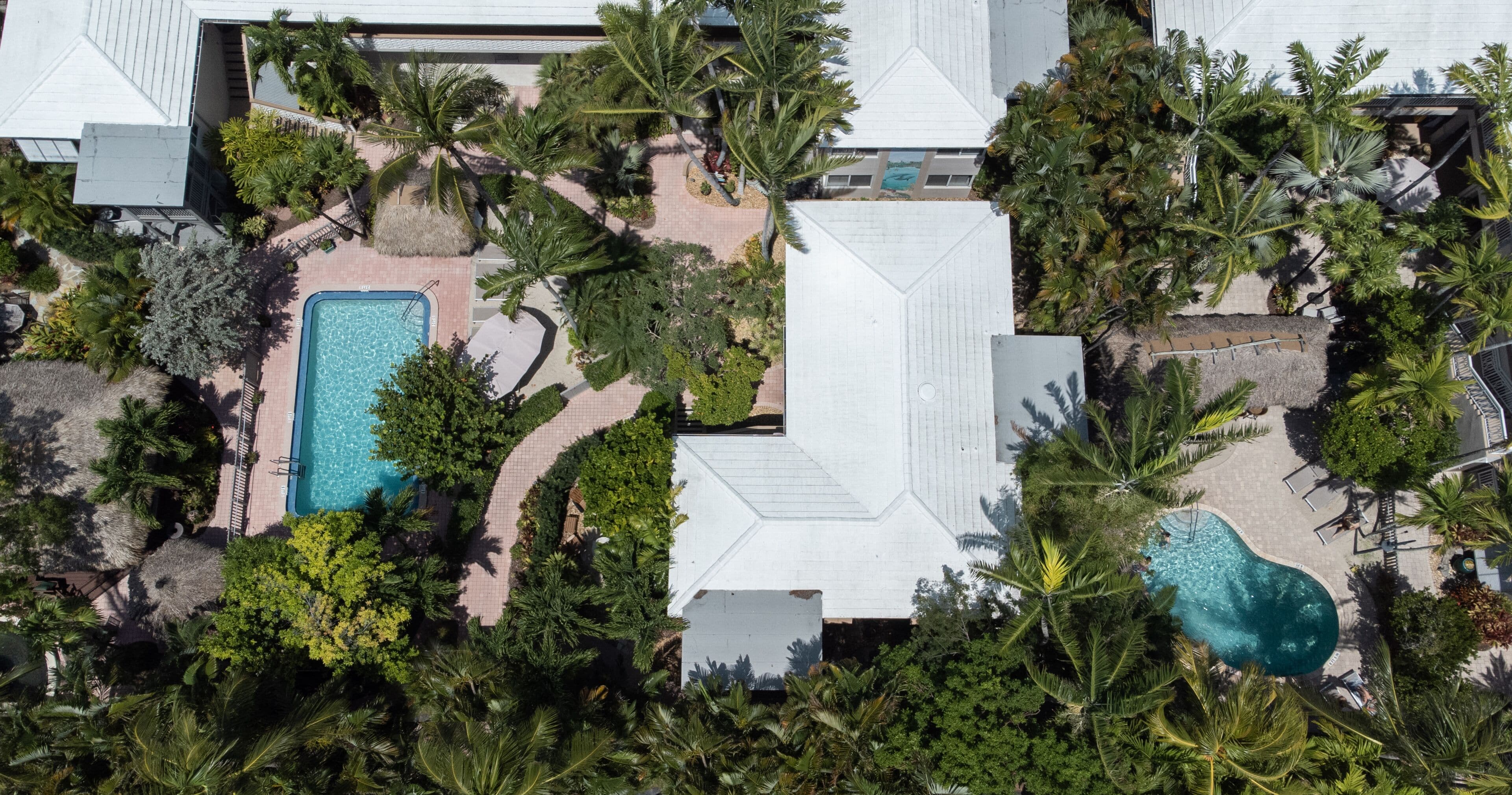 An aerial view of a resort with multiple swimming pools surrounded by lush greenery and palm trees.