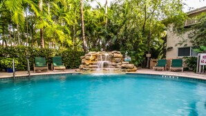 A pool with a waterfall feature surrounded by lush greenery and lounge chairs. - Crane's Beach House Boutique Hotel & Luxury Villas (Delray Beach)