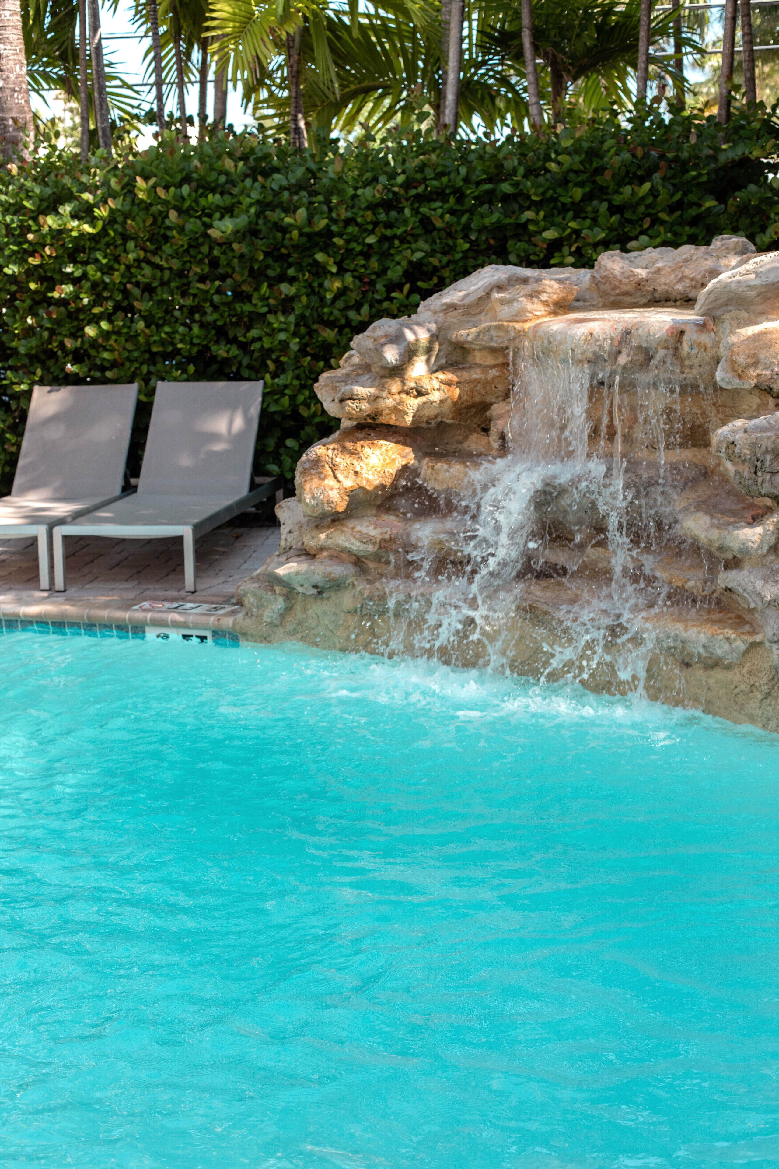 A pool with clear blue water, a rock waterfall feature, and lounge chairs.