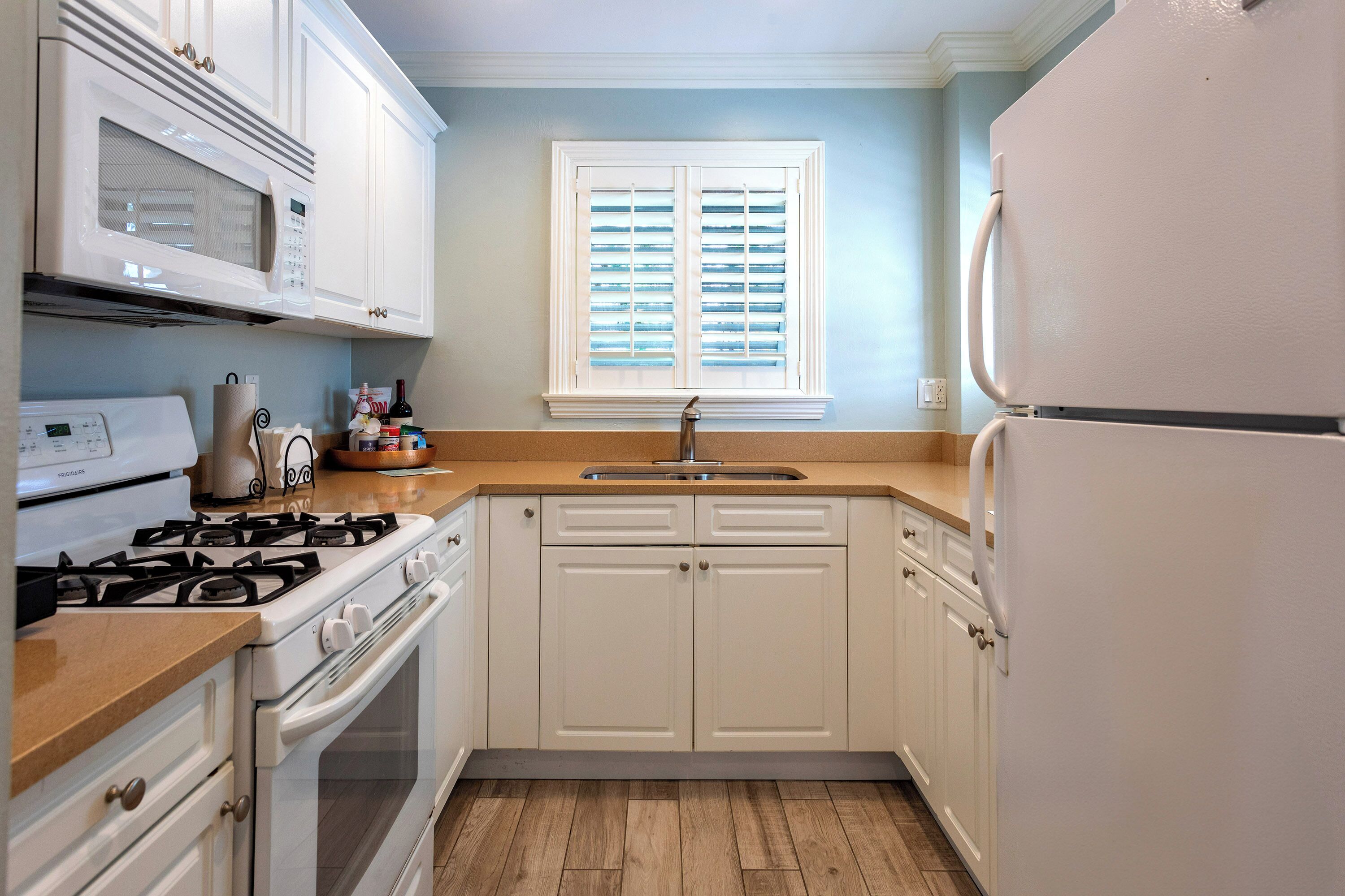 A kitchen with white cabinets, a stove, a microwave, a sink, and a window with blinds.