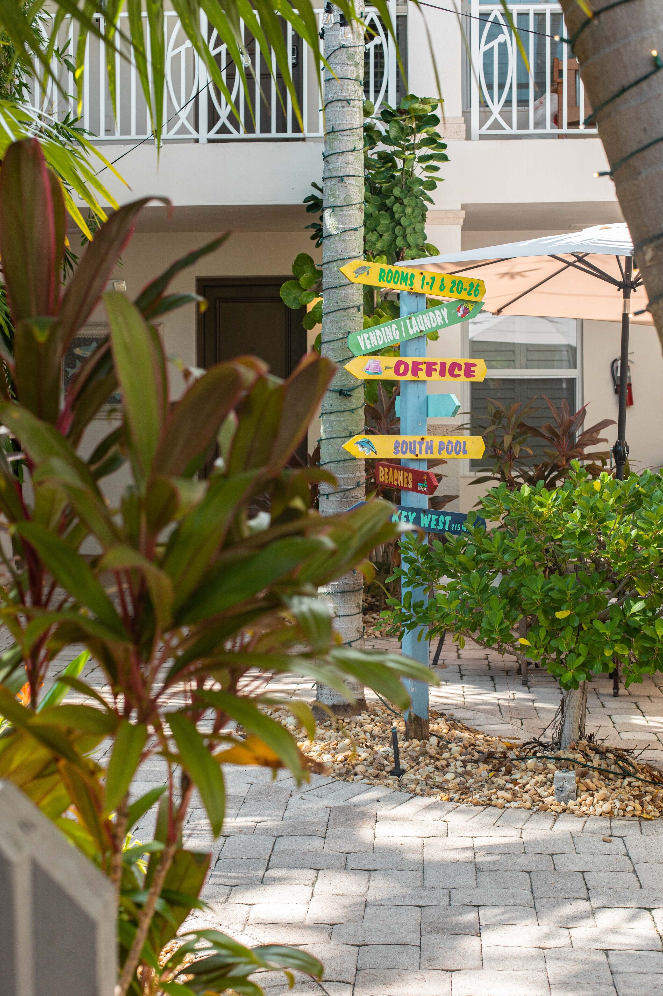 A directional signpost with multiple arrows pointing to various hotel amenities such as rooms, laundry, office, pool, beaches, and a key west area.