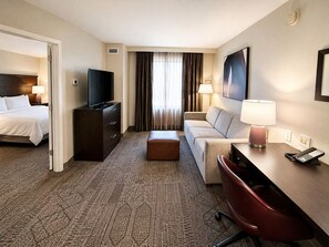 Ein Hotelzimmer mit Bett, Fernseher, Schreibtisch mit Lampe, einer Couch und einem Sessel.
